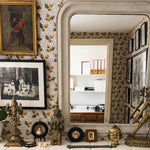 Decorative interior with a large mirror, framed pictures, and ornate statues on a patterned acorn wall.