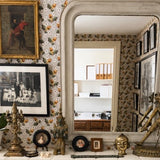 Decorative interior with a large mirror, framed pictures, and ornate statues on a patterned acorn wall.