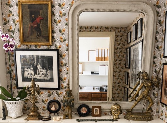 Decorative interior with a large mirror, framed pictures, and ornate statues on a patterned acorn wall.