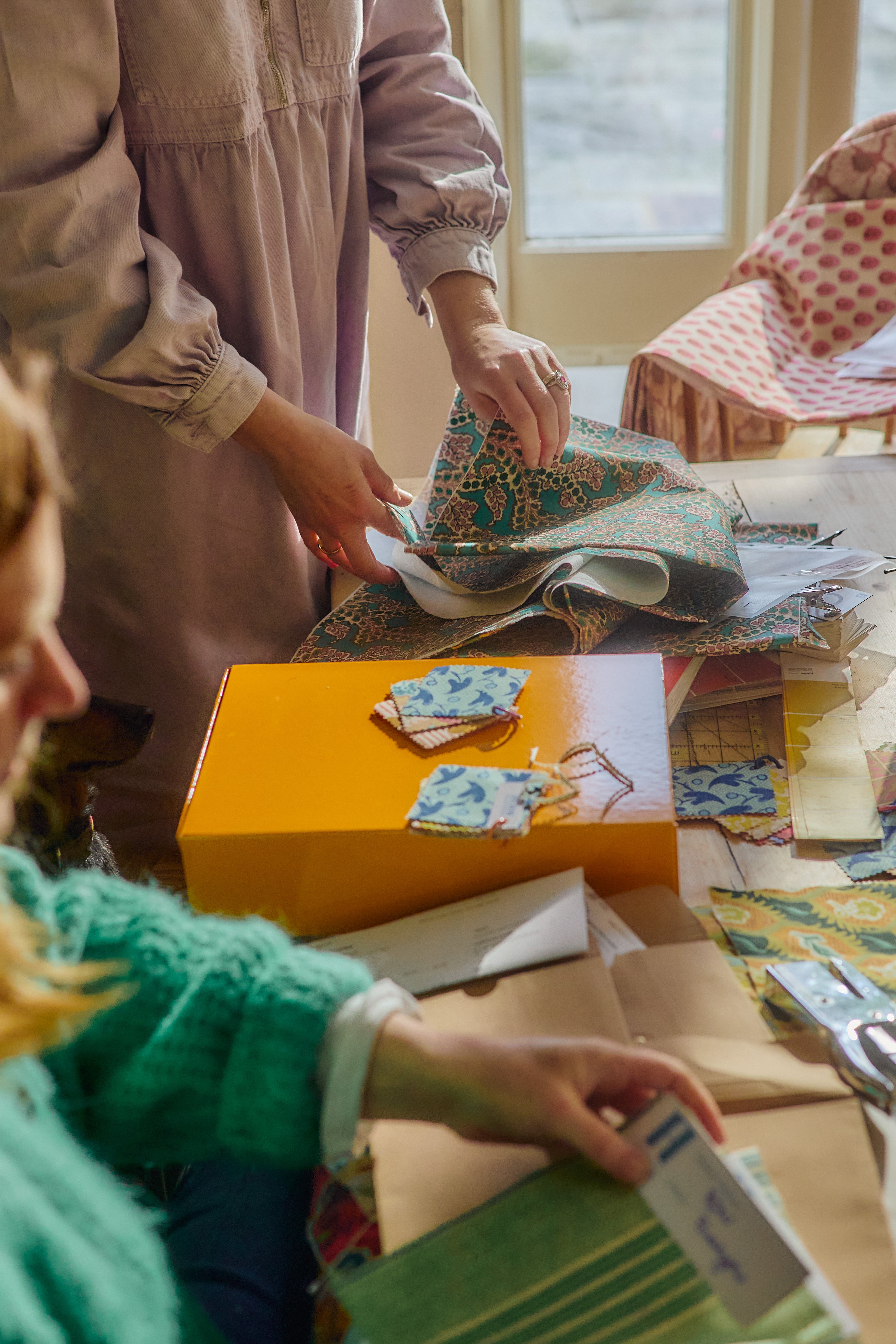 Two people working with fabric SAMPLES on a table in a room with large windows.